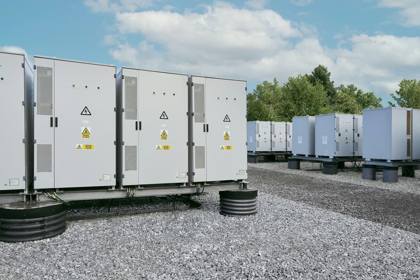 Battery storage units on a gravel site under a blue sky